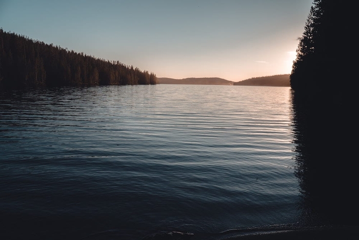 large lake surrounded by trees at sunset.